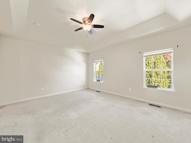 spare room with a raised ceiling, light carpet, and ceiling fan