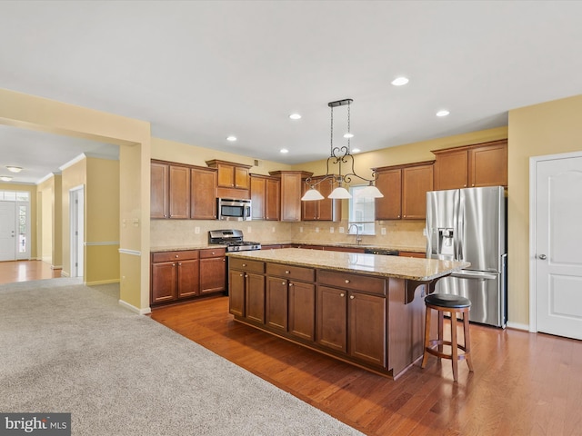 kitchen featuring dark hardwood / wood-style floors, hanging light fixtures, stainless steel appliances, a center island, and a kitchen bar