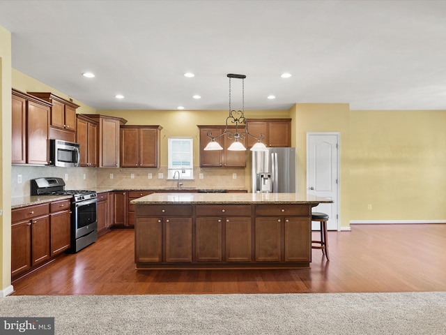 kitchen with dark wood-type flooring, stainless steel appliances, a center island, decorative light fixtures, and light stone counters