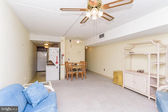 living area with a textured ceiling, baseboards, visible vents, ceiling fan, and light colored carpet