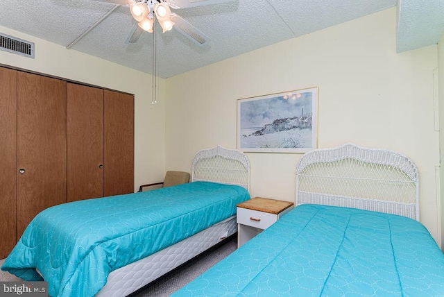 bedroom with a closet, carpet floors, a textured ceiling, visible vents, and ceiling fan