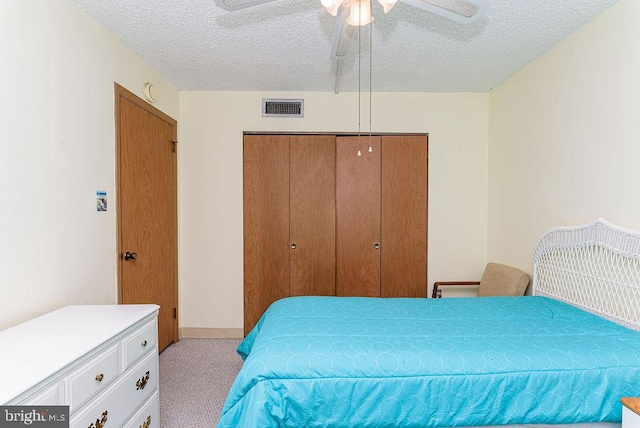 bedroom featuring a closet, a textured ceiling, ceiling fan, visible vents, and light colored carpet