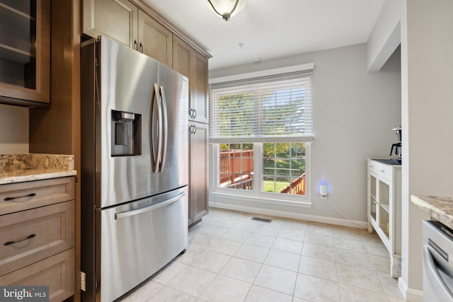 kitchen featuring light stone counters, dishwashing machine, light tile patterned floors, and stainless steel fridge