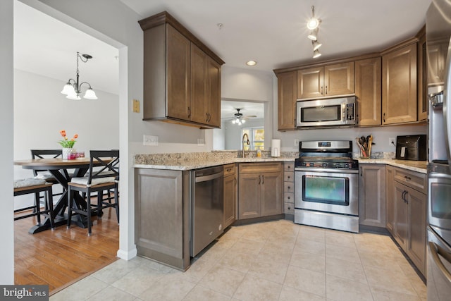 kitchen with appliances with stainless steel finishes, light wood-type flooring, ceiling fan with notable chandelier, pendant lighting, and light stone counters