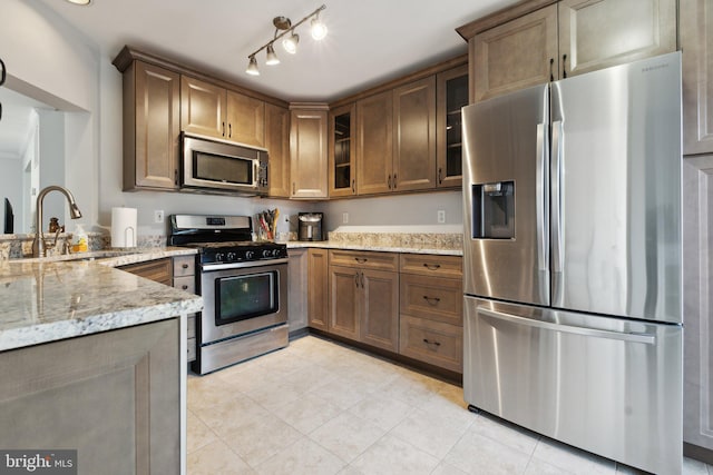 kitchen with kitchen peninsula, stainless steel appliances, sink, light tile patterned floors, and light stone counters