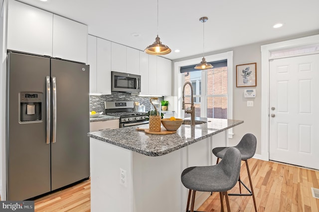 kitchen with hanging light fixtures, light hardwood / wood-style flooring, backsplash, white cabinetry, and stainless steel appliances