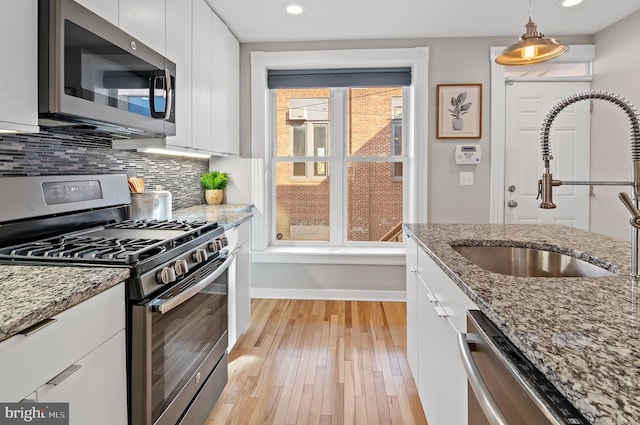 kitchen featuring appliances with stainless steel finishes, pendant lighting, white cabinetry, and sink