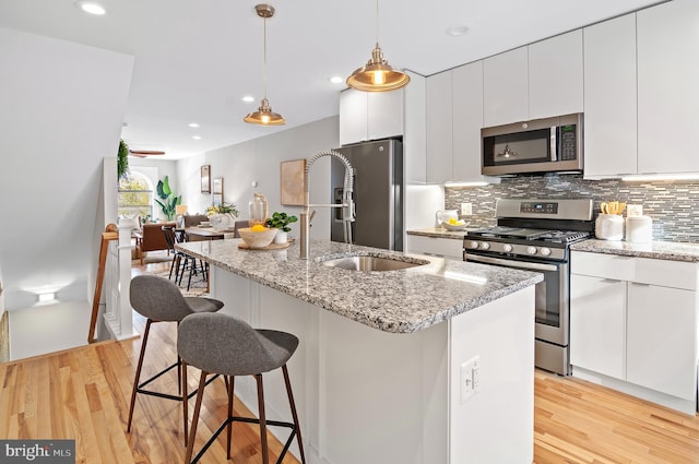 kitchen with light wood-type flooring, a kitchen island with sink, decorative light fixtures, and stainless steel appliances