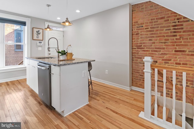 kitchen with light stone counters, stainless steel dishwasher, pendant lighting, white cabinetry, and a center island with sink