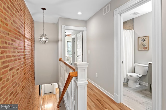 hallway featuring brick wall and light hardwood / wood-style flooring