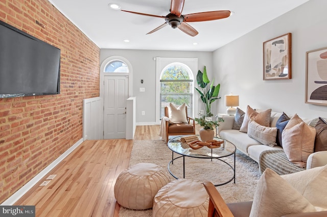 living room with brick wall, light hardwood / wood-style flooring, and ceiling fan