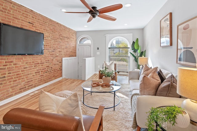 living room featuring brick wall, light wood-type flooring, and ceiling fan