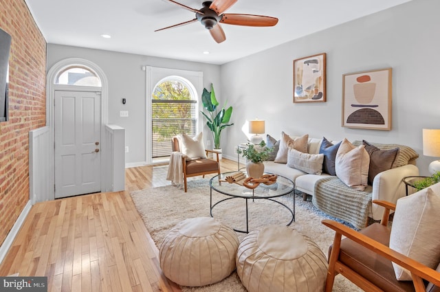 living room with ceiling fan, brick wall, and light hardwood / wood-style flooring