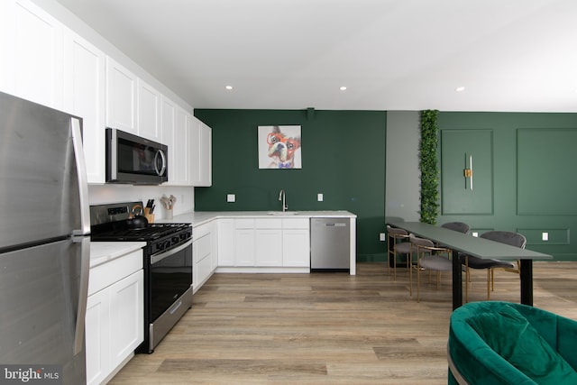 kitchen with light hardwood / wood-style floors, appliances with stainless steel finishes, sink, and white cabinets