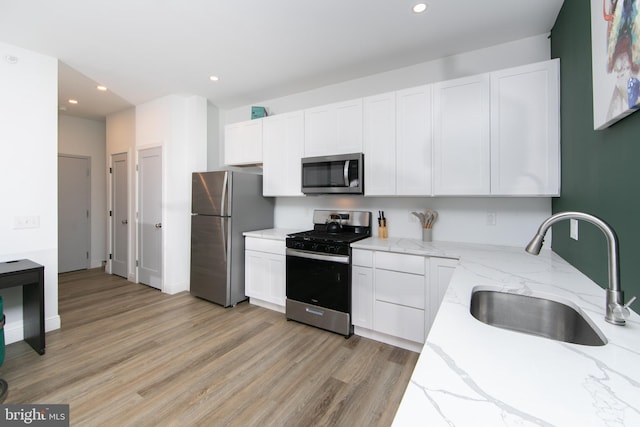 kitchen featuring light stone countertops, sink, white cabinetry, light hardwood / wood-style floors, and stainless steel appliances