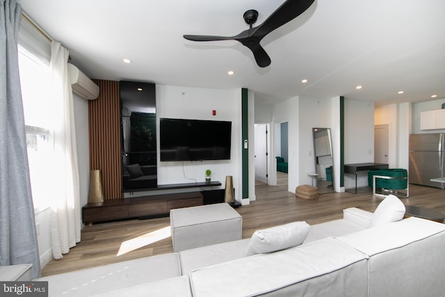 living room with light hardwood / wood-style flooring, a wall mounted AC, and ceiling fan