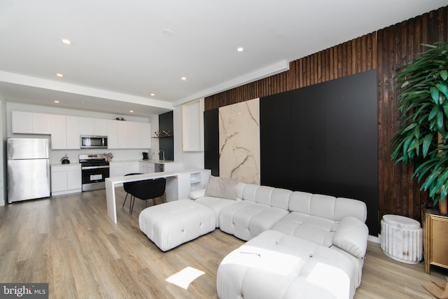 living room with wood walls, sink, and light wood-type flooring