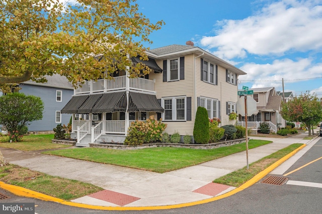 view of front of house featuring a front lawn, covered porch, and a balcony