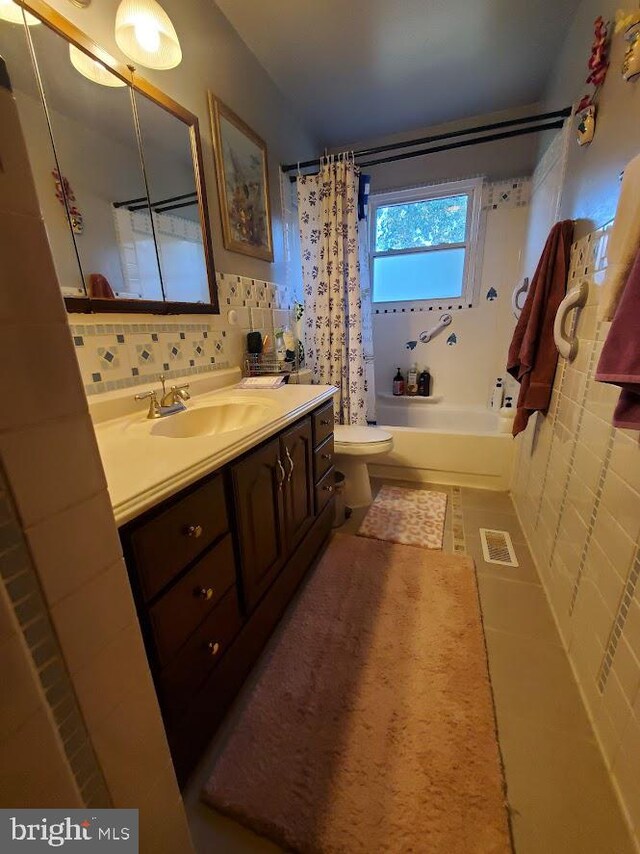 full bathroom featuring vanity, shower / bath combo with shower curtain, tile walls, tile patterned flooring, and toilet