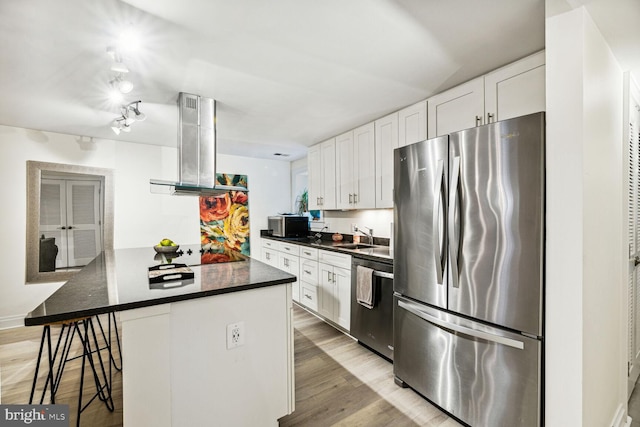 kitchen featuring white cabinets, a kitchen bar, light wood-type flooring, range hood, and stainless steel appliances