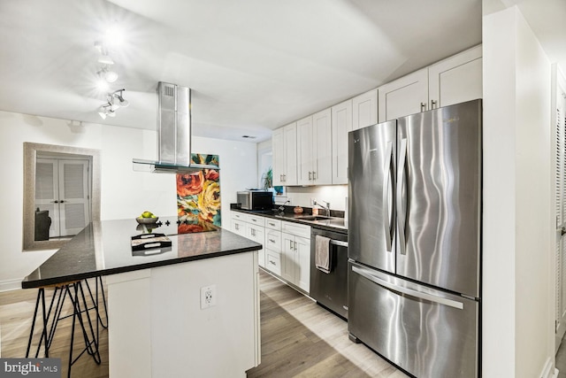kitchen with a kitchen breakfast bar, dark countertops, white cabinetry, range hood, and appliances with stainless steel finishes