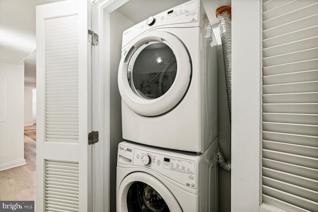 clothes washing area with wood finished floors, stacked washer / dryer, and laundry area
