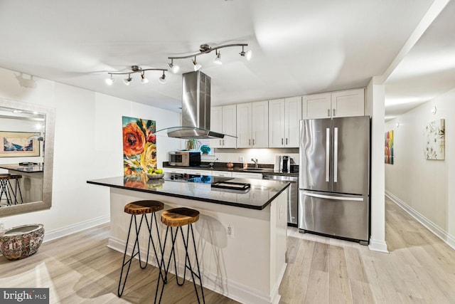 kitchen with island range hood, light hardwood / wood-style floors, stainless steel appliances, white cabinets, and a breakfast bar area