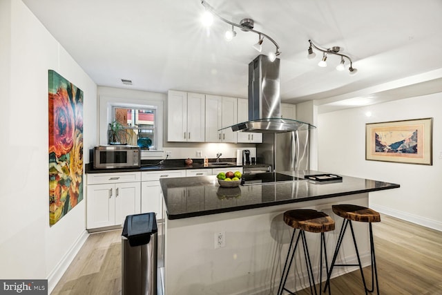 kitchen featuring island exhaust hood, white cabinets, a kitchen island, light hardwood / wood-style flooring, and stainless steel appliances