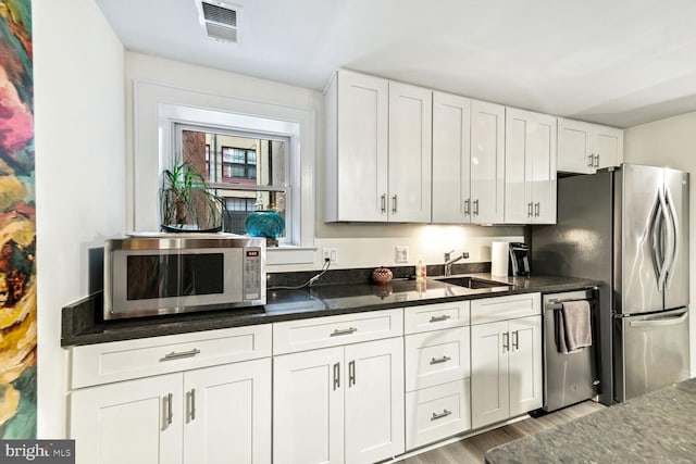 kitchen featuring appliances with stainless steel finishes, white cabinetry, dark stone countertops, light hardwood / wood-style floors, and sink