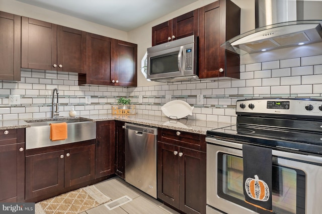 kitchen featuring light stone counters, stainless steel appliances, wall chimney exhaust hood, and tasteful backsplash