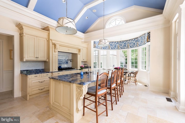 kitchen with dark stone counters, cream cabinets, decorative light fixtures, and a kitchen island with sink