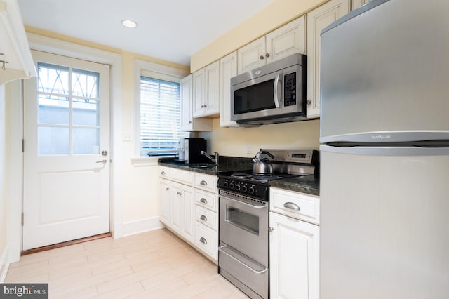 kitchen with dark stone counters, appliances with stainless steel finishes, sink, and white cabinetry