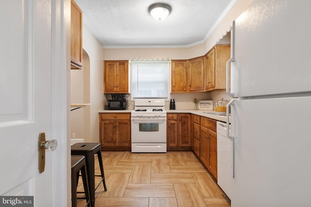 kitchen with ornamental molding, white appliances, and light parquet flooring