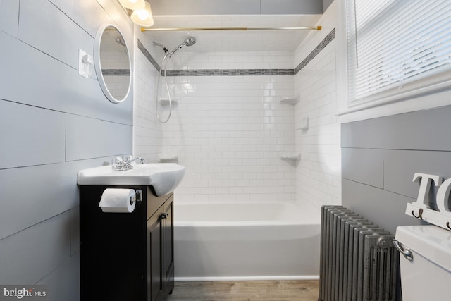 full bathroom featuring toilet, radiator heating unit, tiled shower / bath combo, hardwood / wood-style flooring, and vanity