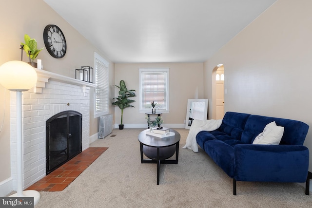 carpeted living room with a brick fireplace and radiator