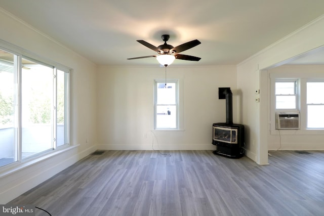 unfurnished room with light hardwood / wood-style floors, a wood stove, ceiling fan, and ornamental molding