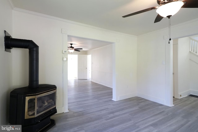 unfurnished living room featuring ceiling fan, a wood stove, crown molding, and light hardwood / wood-style flooring