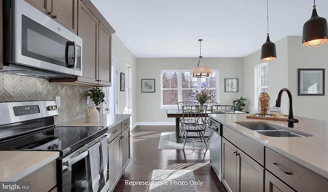 kitchen featuring backsplash, appliances with stainless steel finishes, hanging light fixtures, sink, and dark wood-type flooring