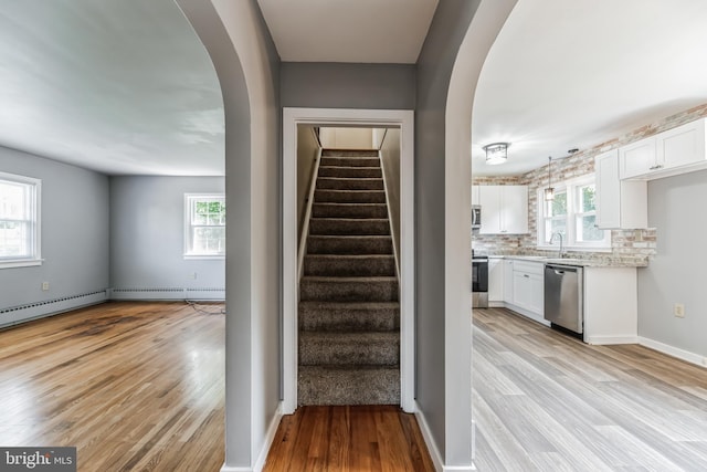 staircase with wood-type flooring, sink, and a baseboard heating unit