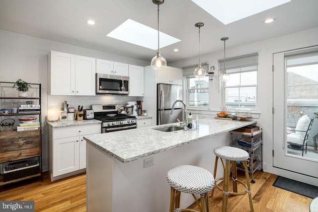 kitchen with sink, light hardwood / wood-style flooring, a skylight, white cabinetry, and stainless steel appliances