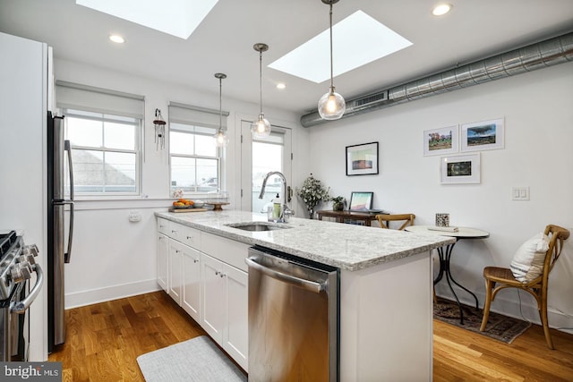 kitchen with a skylight, light stone counters, stainless steel appliances, white cabinets, and light hardwood / wood-style floors