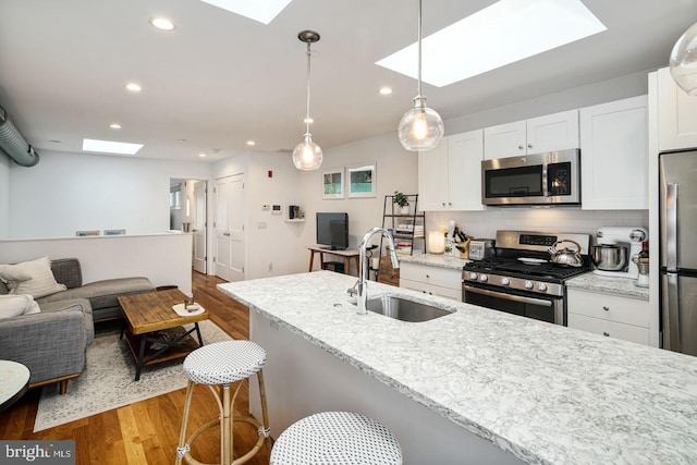 kitchen with a kitchen breakfast bar, sink, light stone countertops, white cabinetry, and stainless steel appliances