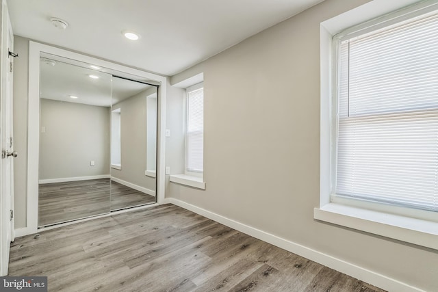 unfurnished bedroom with a closet, multiple windows, and light wood-type flooring