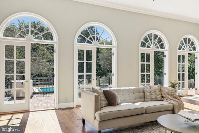 living room featuring ornamental molding, light wood-type flooring, a healthy amount of sunlight, and french doors