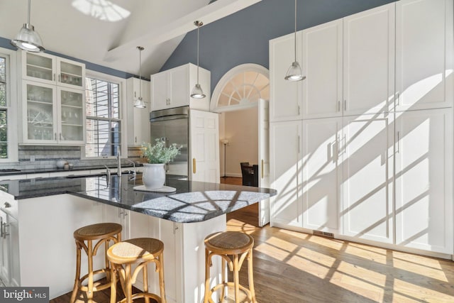 kitchen featuring built in fridge, decorative light fixtures, vaulted ceiling, and white cabinetry