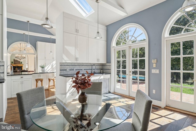 dining area featuring a skylight, sink, french doors, high vaulted ceiling, and light wood-type flooring