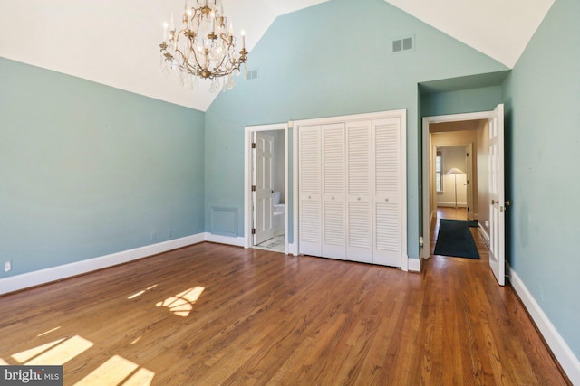 unfurnished bedroom with hardwood / wood-style flooring, a closet, a notable chandelier, and high vaulted ceiling