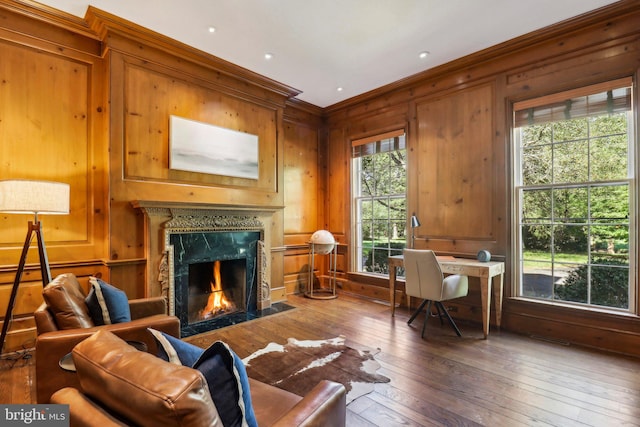 sitting room with a fireplace, hardwood / wood-style flooring, wooden walls, and a healthy amount of sunlight