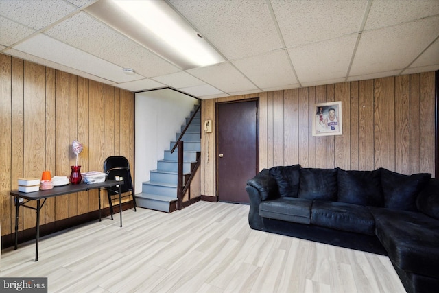 living room with a drop ceiling, wood walls, and wood-type flooring