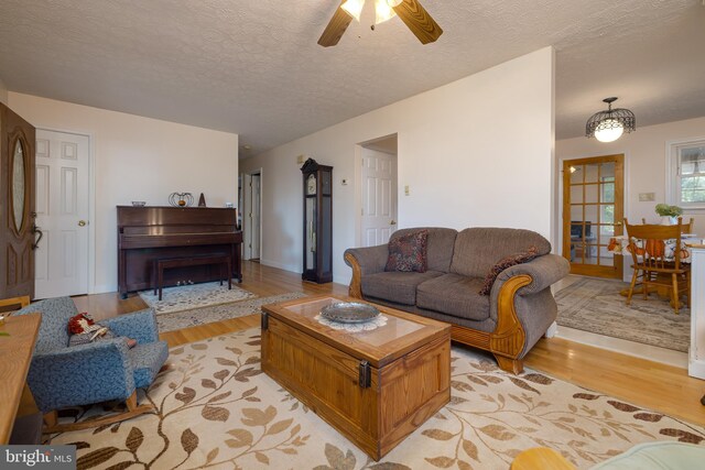 living room with ceiling fan, a textured ceiling, and light hardwood / wood-style flooring